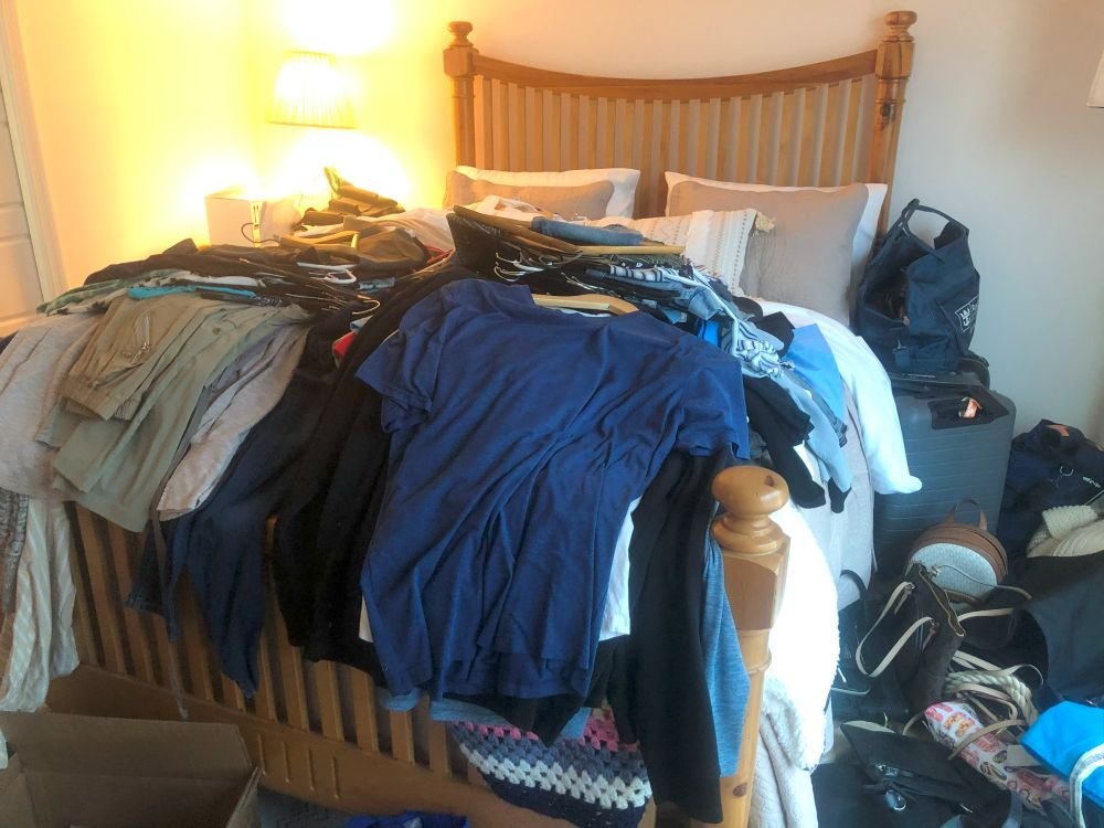 A cluttered bedroom scene with clothes piled high on a bed, illustrating the starting point of a closet decluttering project.