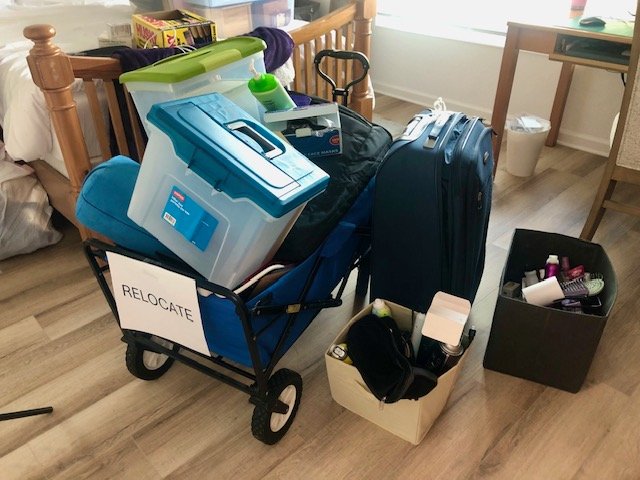 A blue wagon filled with storage bins, bags, and household items labeled “Relocate” as part of the 12-12-12 declutter process.