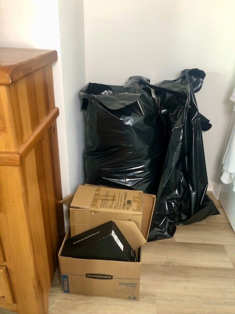 Large black garbage bags and cardboard boxes stacked neatly in a corner after decluttering a guest bedroom.