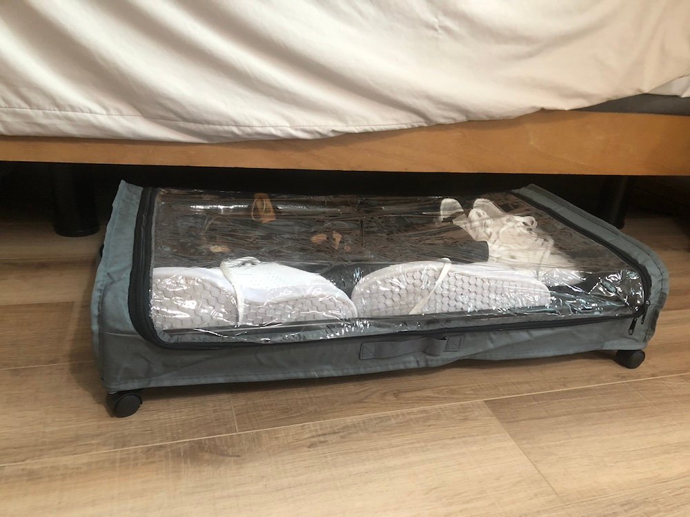 A rolling under-bed bin with a transparent lid, filled with neatly folded clothing—perfect for out-of-season items or spare linens.