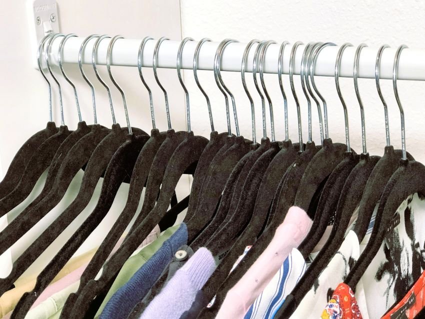 A row of black velvet hangers on a closet rod holding neatly arranged clothing, showing a simple solution for how to organize your closet with uniform hangers.